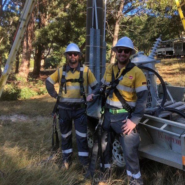 {cf_related_case_studies2 Powercor employees in their uniforms, wearing harnesses and hardhats in preparation for climbing a power pole.